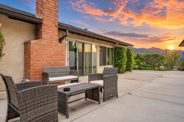 Gated white stucco California home with palm trees, manicured hedges and a black iron gate.